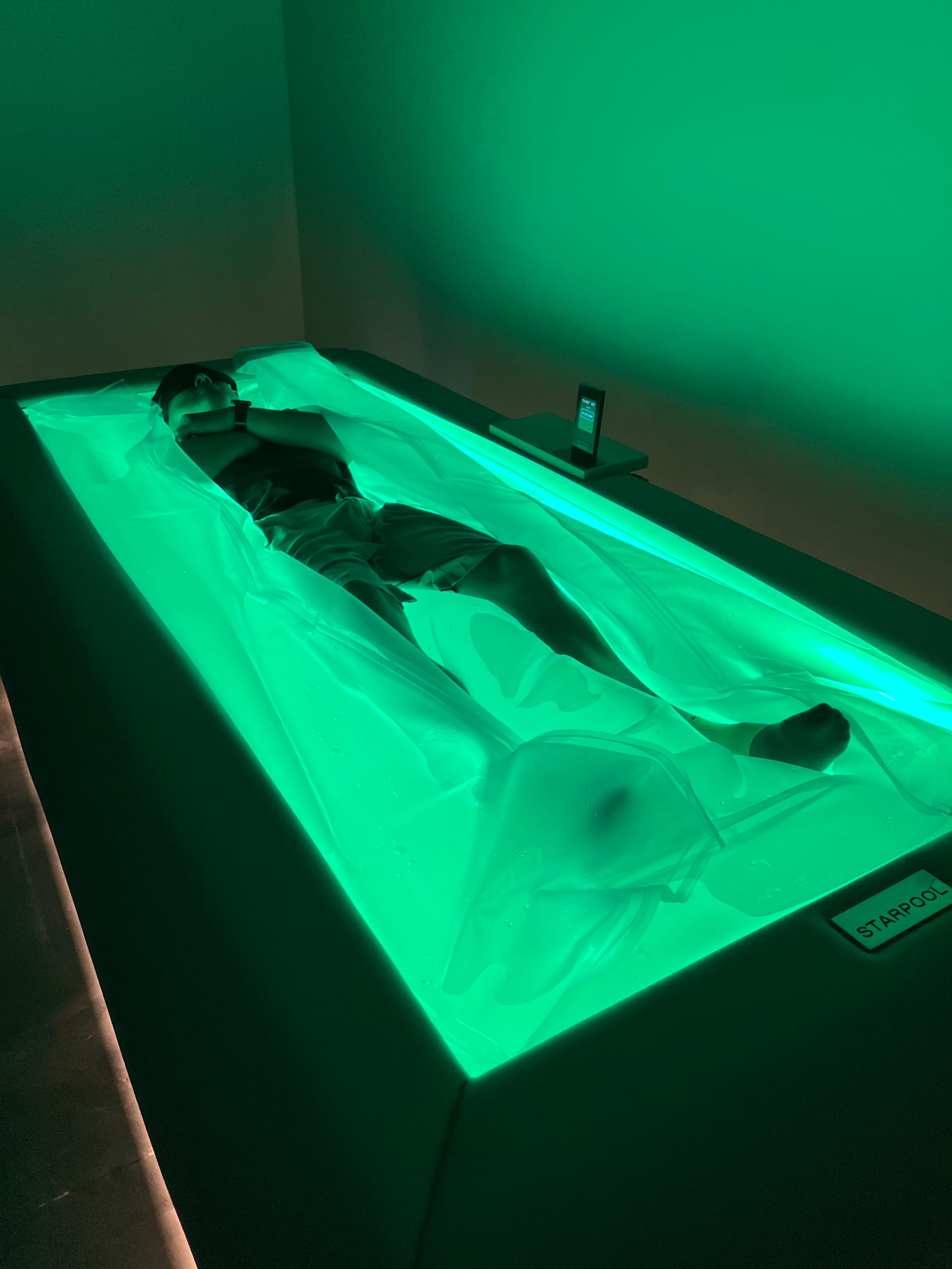 Client relaxing on Starpool dry float bed with green ambient lighting at Zivel